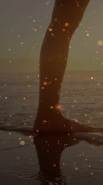 Vertical video: Foot touching sand, woman walking, toes splashing, relaxing under golden particles
