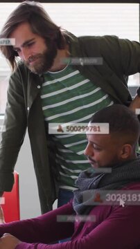 Vertical video: Pair leaning over laptop, pointing and using mouse, business data overlays aligning