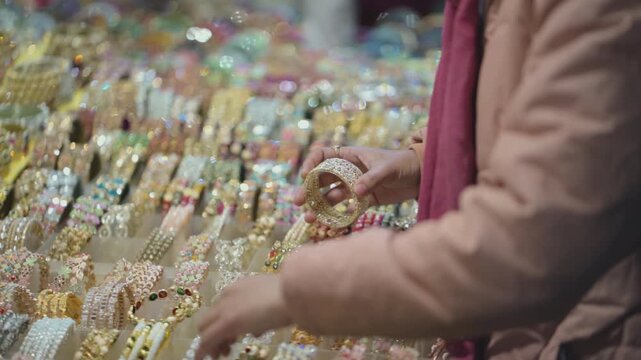 Woman buying bangles at fair market, Indian mela bangle shopping close up, Traditional bangles selection in local market, Female hands choosing colorful bangles stock video.