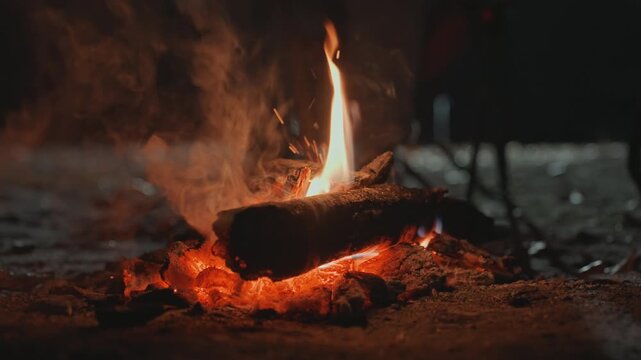 Closeup of glowing embers on burning log, molten coals and ash forming textured surface, flickering orange flame and smoke, atmospheric nighttime campsite detail with warm radiance