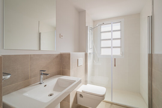 Modern bathroom with a shower, sink, and toilet. Bright lighting and neutral colors create a clean and spacious atmosphere.
