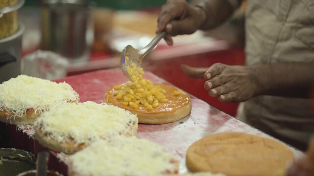 Adding corn topping on pizza base, Street style pizza making with toppings, Fresh pizza preparation with corn and cheese, Handmade pizza topping process close up stock video.