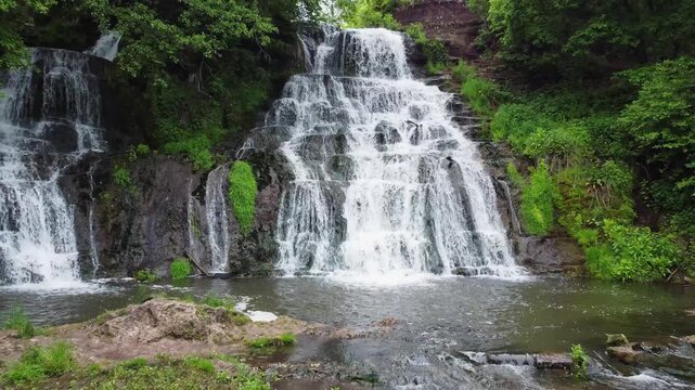 Branches of cascade waterfall among trees in spring overcast day