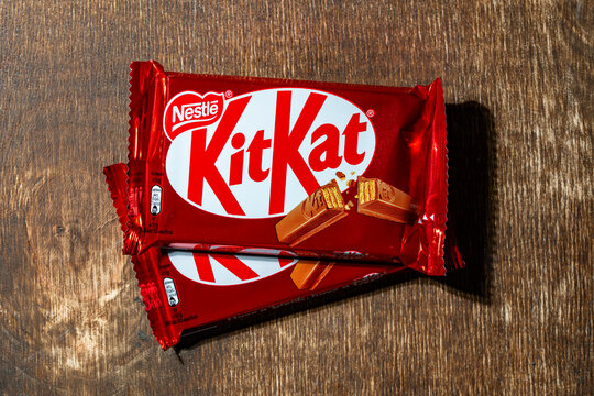 Two Nestle classic red Kit Kat chocolate bars stacked on a rustic wooden table. Crispy wafer snacks in bright foil packaging, perfect for food and retail concepts
