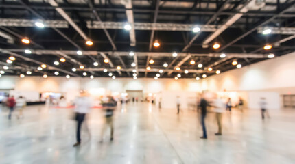 Fototapeta premium Blurred view of people walking through a large exhibition hall with industrial ceiling lights