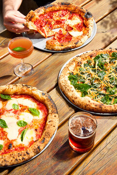 outdoor sunny setting with three pizzas and cocktails
