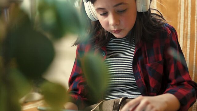  Responsible preteen girl in headphones using tablet to learn about houseplant care at home - 4k, 10bit footage.
