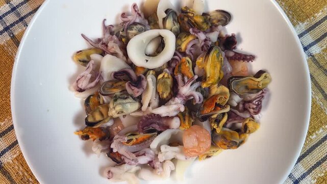 Mix of boiled seafoods in white bowl on checkered napkin