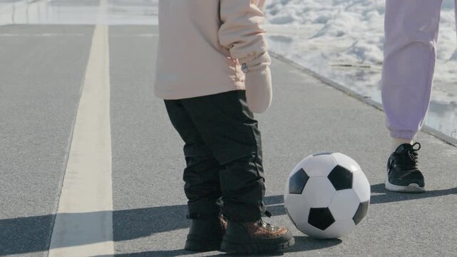 Kids practice football on a cold day with snow on the ground near a paved road and an adult supporting them
