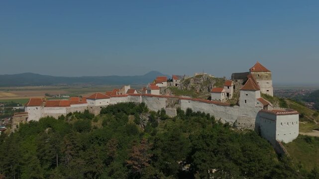 Majestic historic Rasnov Citadel with beautifully reconstructed exterior white walls and red roofs, picturesque pulling back wide aerial view with empty sky copy space, graded