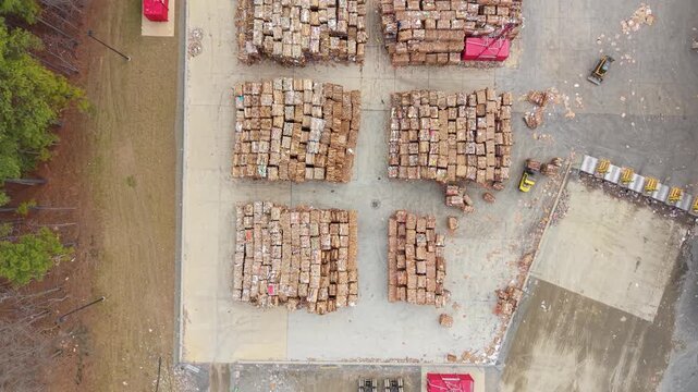 Industrial paper mill recycling yard, featuring massive organized stacks of baled recycled cardboard ready for processing. Aerial top-down tracking video.