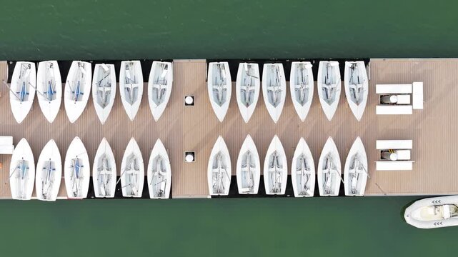 Competitive sailing team dock featuring rows of white racing sailboats organized for practice and regatta preparation. Aerial top-down video.