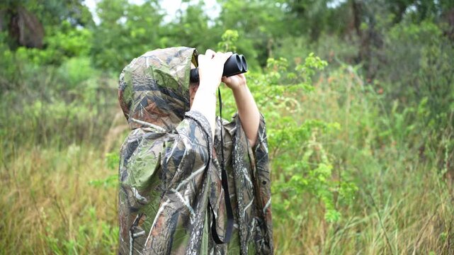 A person wearing a camouflage jacket observing through binoculars