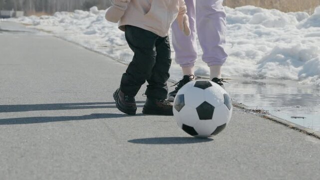 Child practices soccer skills on a street with a black and white ball while wearing winter clothing