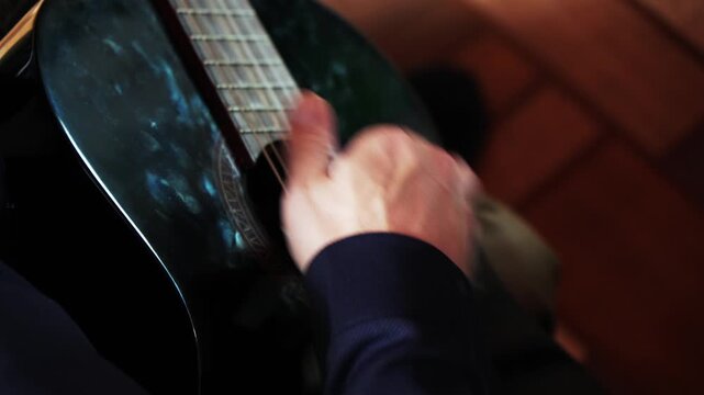 Close view of a hand playing guitar strings in a cozy room during a music practice session