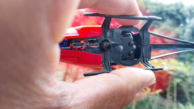 Macro view of hand holding small red toy helicopter showing interior mechanics and charging port clip.