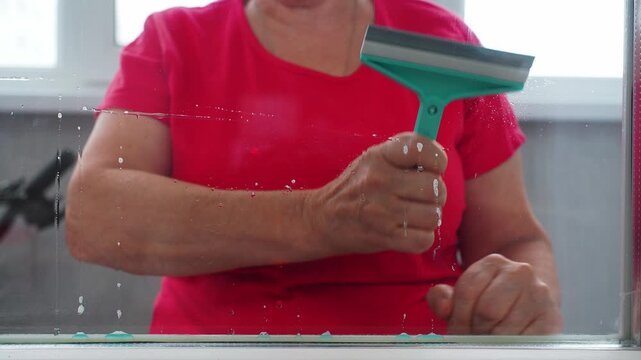 A person stands near a window in a home. They use a squeegee to clean the glass