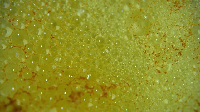 Extreme close up of a citrus flavored effervescent tablet dissolving in water, creating vibrant yellow bubbles foam
