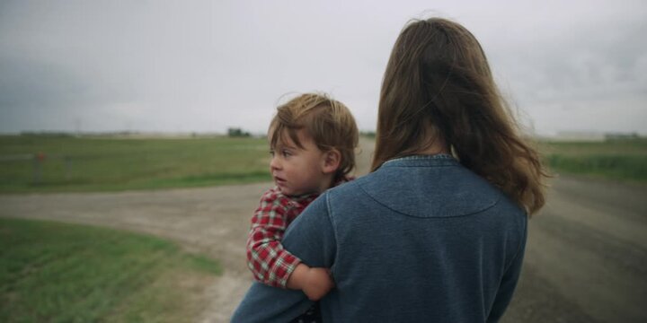 Mother holding a toddler close in a rural countryside setting