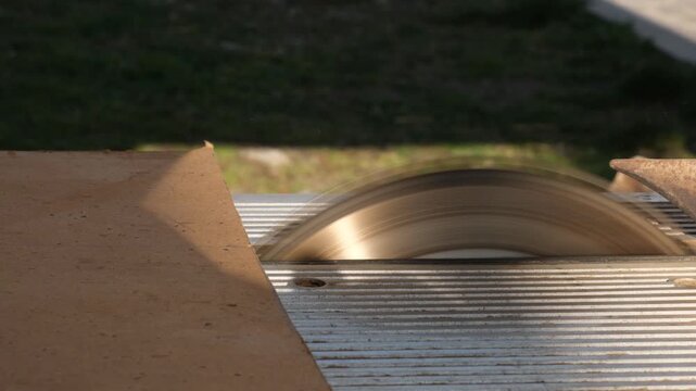 Thin hardboard sheet approaches spinning circular saw blade and begins to be cut by sharp teeth. Cutting plywood with electric circular saw outdoors. Production and assembly of custom furniture.
