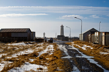 Obraz premium Scenic view of Akranes lighthouses at the end of a rural road with snow and puddles under a clear blue sky, Iceland