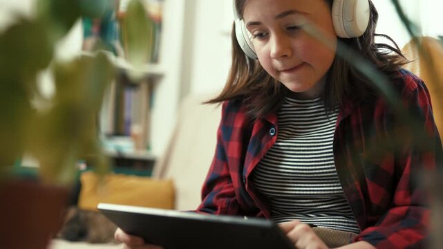  Responsible preteen girl in headphones using tablet to learn about houseplant care at home - 4k, 10bit footage.