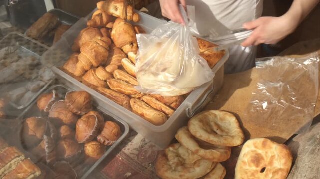 Street bakery seller packs several hot pita breads and one sweet muffin into a bag. Selling tasty hot bread in bakery and pastry shop. Traditional national bread baked in tandoor and stone oven