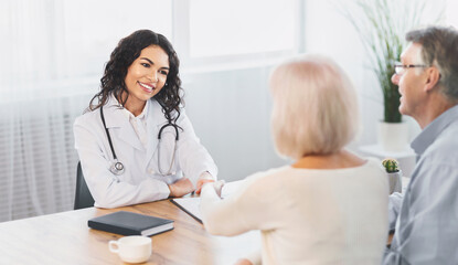 Naklejka na ściany i meble General Practitioner. Mexican woman physician and senior couple patients handshaking at doctor's office, copy space