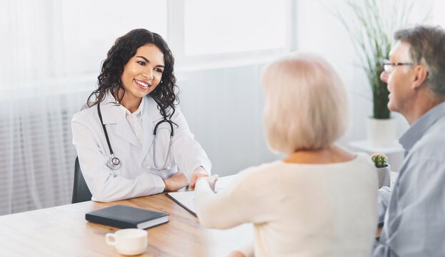 General Practitioner. Mexican woman physician and senior couple patients handshaking at doctor's office, copy space