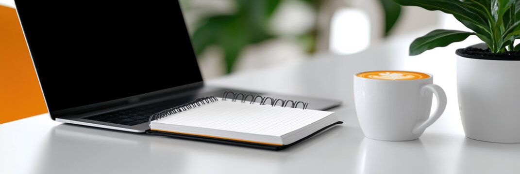 Minimalist workspace setup with an open laptop displaying a blank screen. An open spiral notebook for note making. A takeaway coffee cup. And a green potted plant on a clean white desk