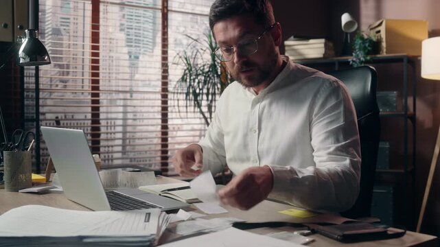 Stressed sad Caucasian middle aged business man holding bills reading paper computer in office accountant male businessman counting costs money loss laptop data problem finance bankruptcy taxes indoor