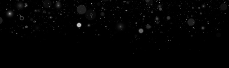 White glitter sparkles flow like magic dust. Soft bokeh highlights illuminate the dark background. Perfect for Christmas, winter, and holiday designs. © goldstock