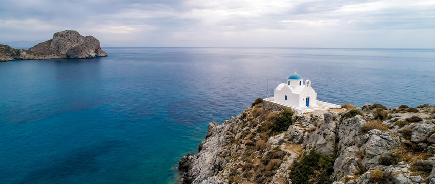 White chapel on cliff with blue dome overlooking aegean sea