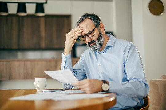 Worried man calculating bills and struggling with financial stress at home
