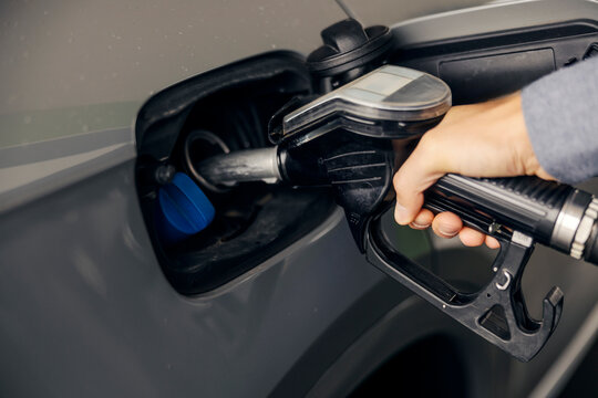 Hand holding fuel nozzle refueling vehicle at gas station