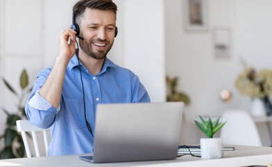 Hotline Operator. Handsome Man Customer Support Manager In Headset Working With Laptop Computer In Office, Consulting Clients Online, Managing Issues, Sitting At Desk, Free Space