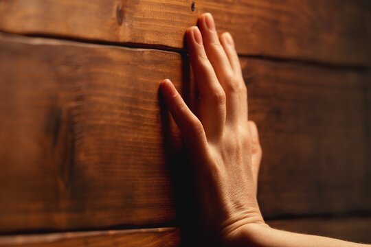 Macro shot of female hand touching natural grunge weathered wooden wall. Selective focus on human skin and wood grain texture. Soft bokeh background with copy space. Rustic and contrast backdrop.
