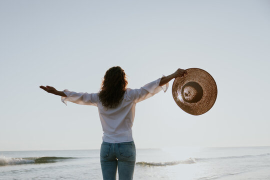 Young happy woman enjoys the summer sun on the beach during the sunrise