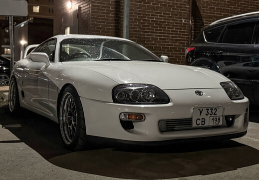 White Japanese sport car Toyota Supra IV A80 3.0 AT Turbo Sport Roof  at night the city street. Exterior of a Japanese two-door sport coupe Toyota Supra Turbo IV on parking lot. The legendary JDM car.