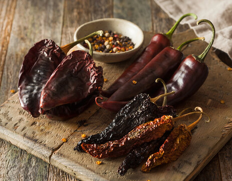 Dried chili pepper varieties, including ancho, guajillo, and chipotle, displayed on wood.