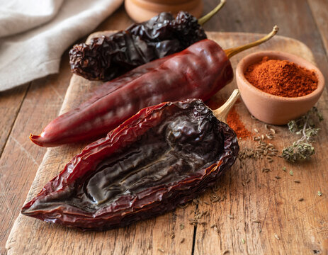 Dried chili pepper varieties, including ancho, guajillo, and chipotle, displayed on wood.