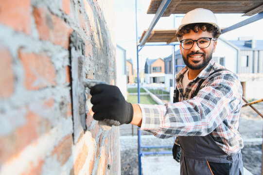 African american construction worker smiling while plastering brick wall