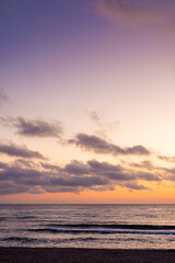 Obraz premium sunrise over the sea. beach landscape in golden glow. morning sky with purple clouds above horizon. scenery with calm waves. tranquil seascape wallpaper for summer vacation