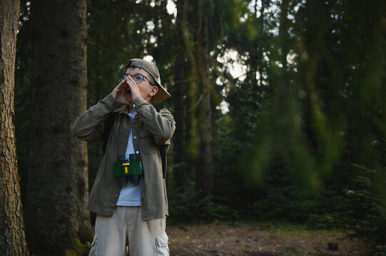 Young explorer shouting for help in forest wearing binoculars