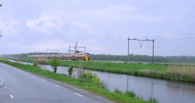 Lisse, Netherlands - May,12,2023: Dutch intercity train passing a windmill in the countryside