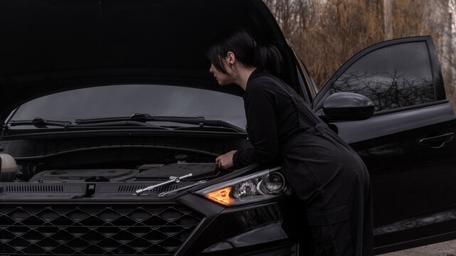 female mechanic in work uniform looking under the hood of a car with smoke coming from it before repair. smoke from the engine, smoke from the battery, emergency stop, repair, problem, headlight