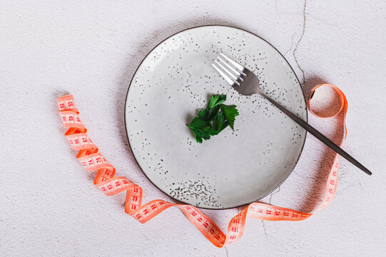 Close up of parsley leaves and a fork on an empty plate, a notebook and capsules top view