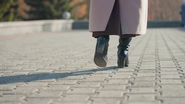 Autumn city walk features. Walking shoes on patterned cobblestones. Pavement journey under long coat during autumn. Confident stride over cobblestones beneath long coat in autumn city lights