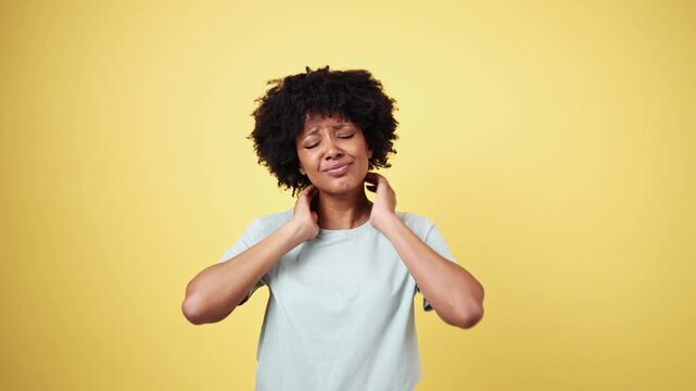 Young woman suffering from neck pain on yellow background