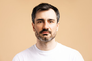 Obraz premium Portrait of handsome, pensive man looking at camera posing isolated on beige background